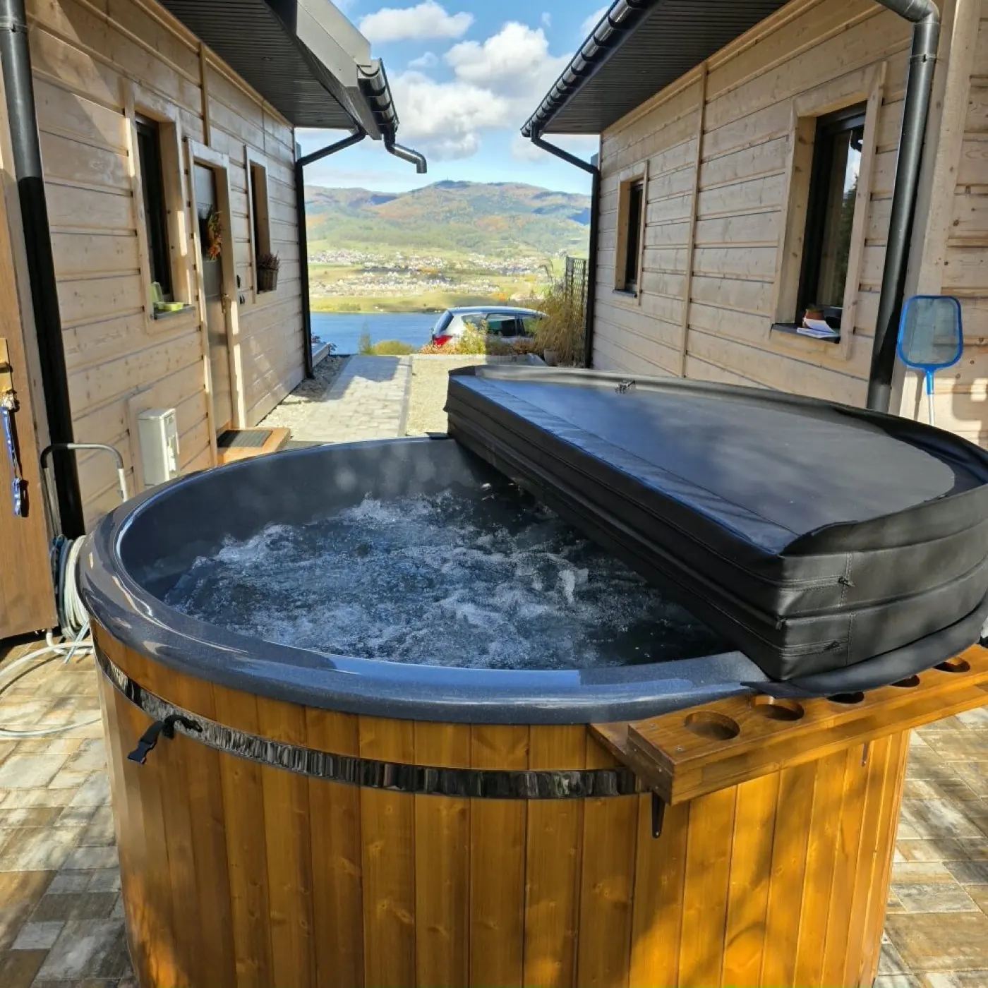 Wanna SPA ogrodowa Wójciak SPA z otwartą pokrywą termiczną, ustawiona przy drewnianym domu z widokiem na góry