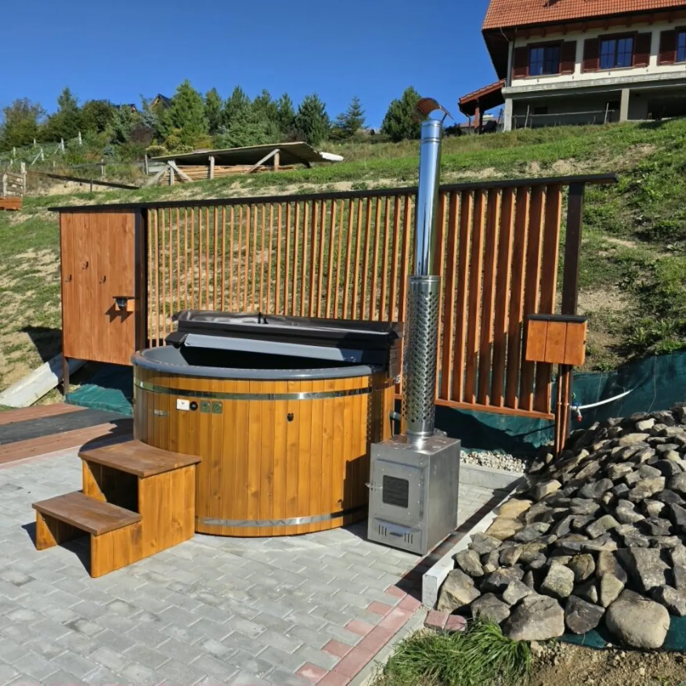 Balia ogrodowa z zewnętrznym piecem na drewno ze stali nierdzewnej, zamontowana na skarpie przy domu